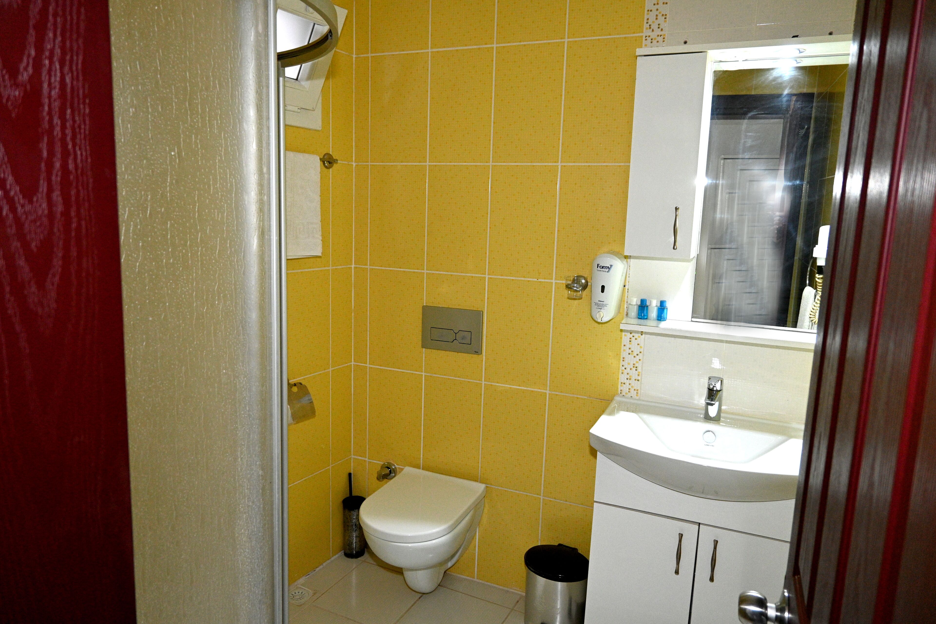 A small bathroom with yellow tiles, a white toilet, a sink, and a trash can.
