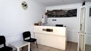 A reception area with a reception desk labeled "RECEPTION," a clock, and a wall-mounted photo. - Melis Pansiyon (Bodrum)
