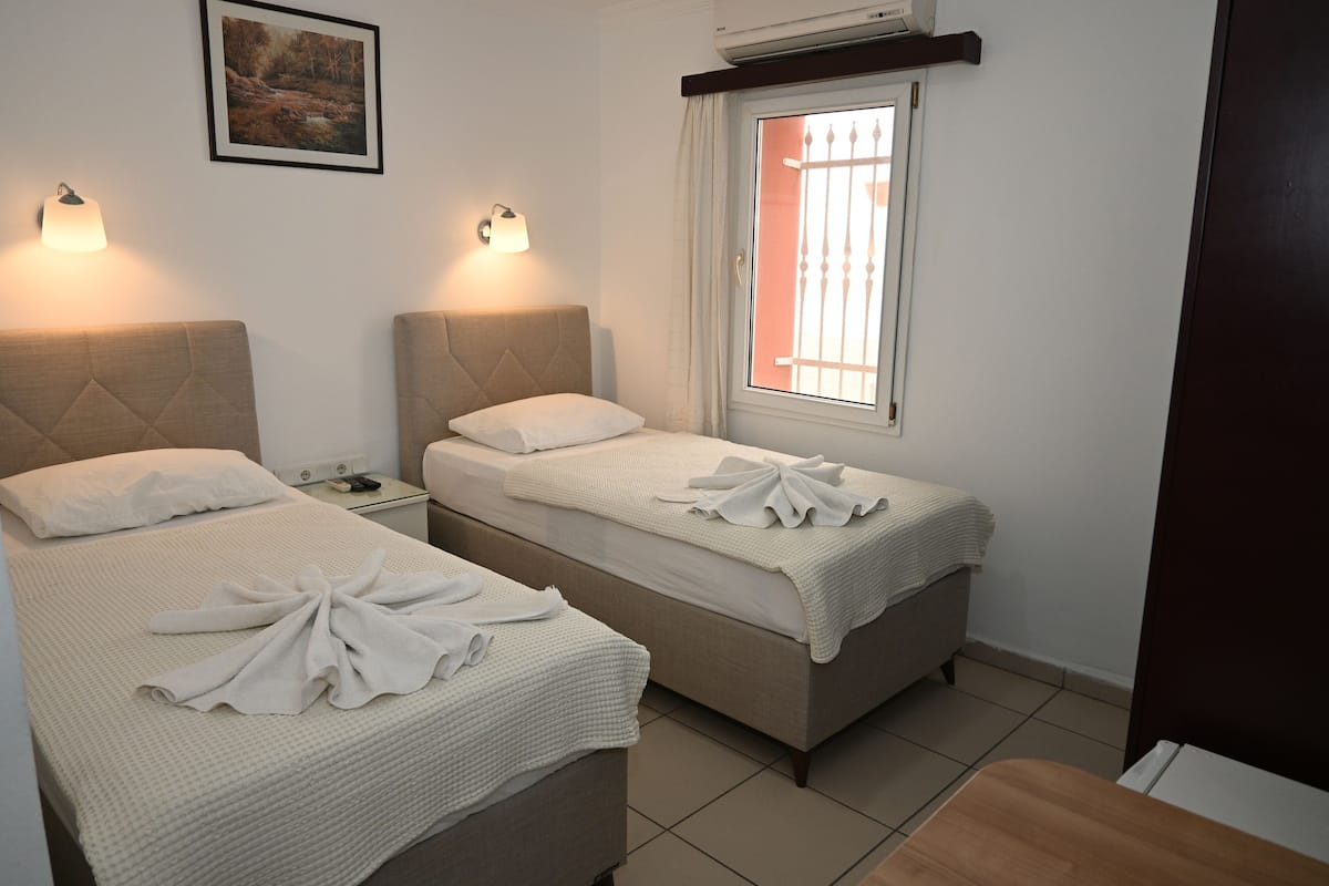 A hotel room with two beds, a nightstand, a window with bars, and a painting on the wall.