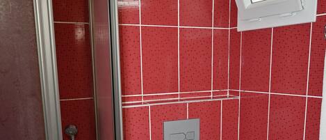 A bathroom with red tiled walls, a white toilet, a white sink, and a shower with a glass door.