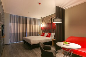 A hotel room with a bed, a red sofa, a small table with fruit, a lamp, and a TV. - ibis Lanzhou Zhangye Road (Lanzhou)