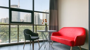 Une pièce moderne avec une grande fenêtre, un canapé rouge, un fauteuil noir et une petite table sur laquelle est posé un vase de fleurs.