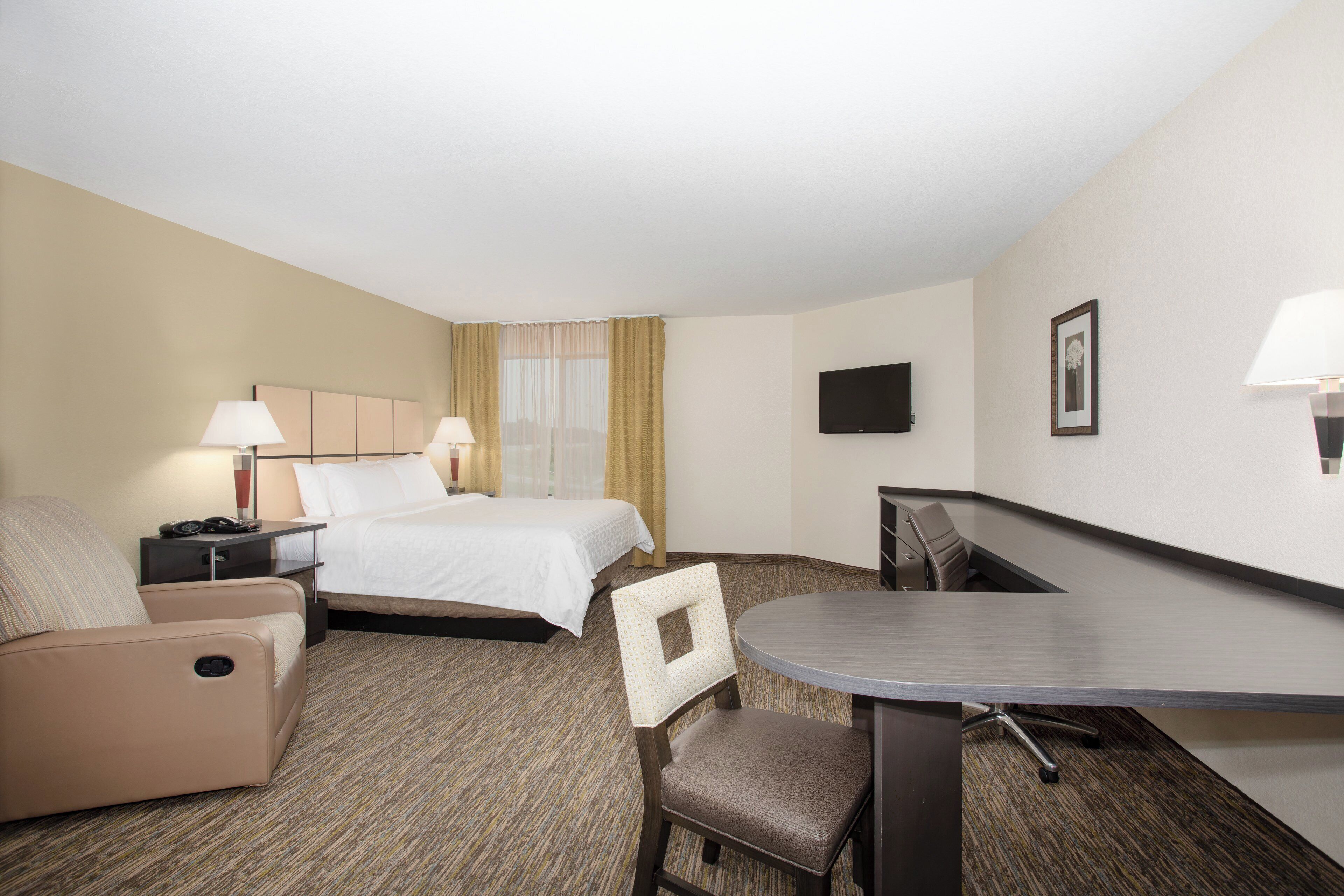 A hotel room with a bed, a desk, a chair, a lamp, a TV, and a carpeted floor.
