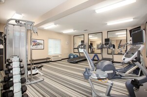 Un gimnasio con equipo de ejercicio, espejos y un ventanal con persianas.
