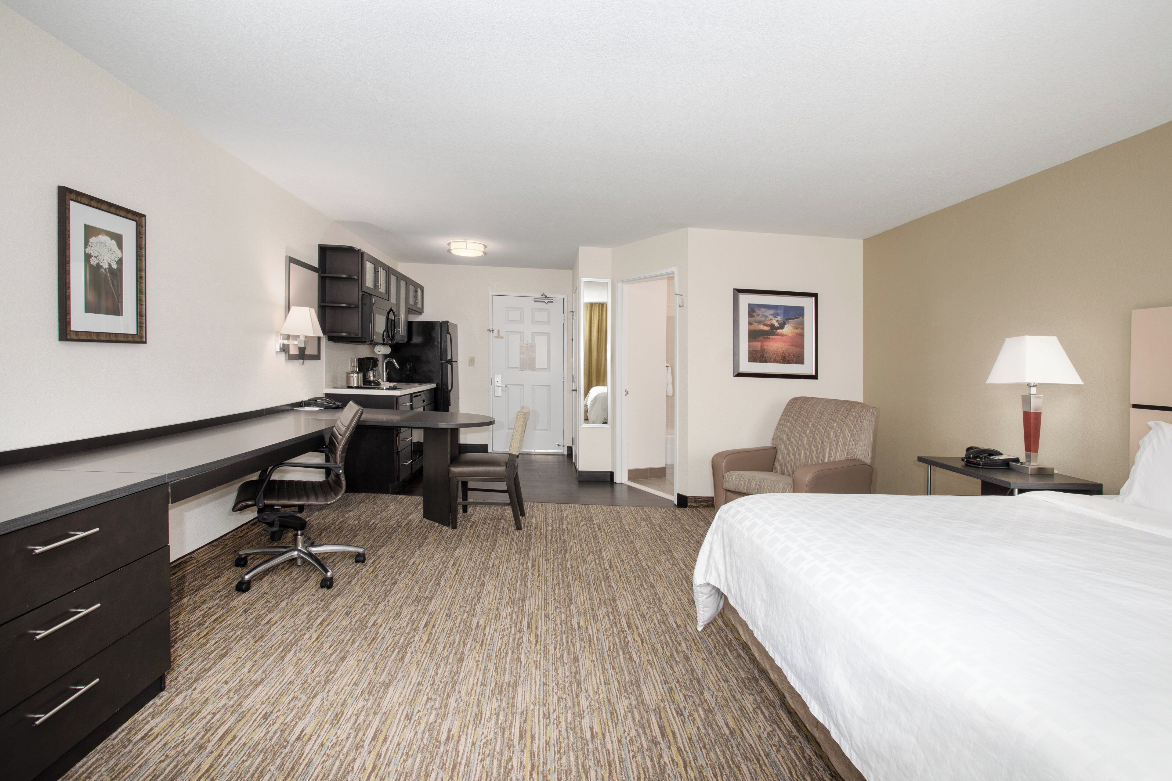 Une chambre d’hôtel comprenant un lit, un bureau, une chaise, une kitchenette et une porte donnant sur une autre pièce.