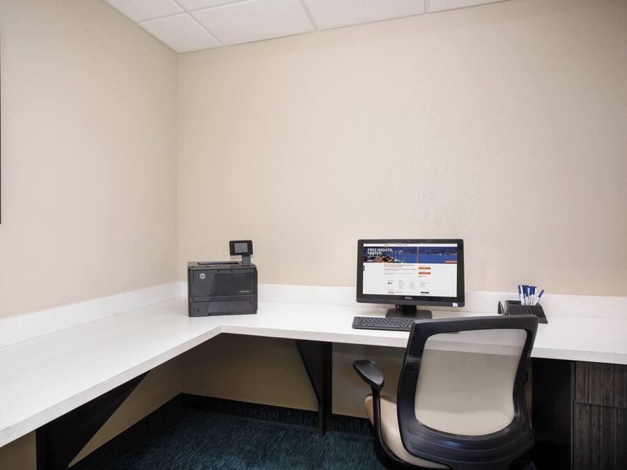 A hotel office with a desk, computer, chair, and a framed picture on the wall.