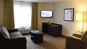 Ein Hotelzimmer mit einer Couch, einem kleinen runden Tisch, einem an der Wand befestigten Flachbildfernseher, einem Schrank und einer Lampe.