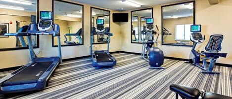 Ein Fitnessstudio mit Laufbändern, Crosstrainern und Fahrrädern, ausgestattet mit digitalen Bildschirmen und Spiegeln.