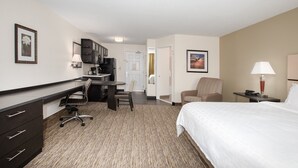 A hotel room with a bed, desk, chair, kitchenette, and a door leading to another room. - Candlewood Suites Manhattan by IHG (Manhattan)