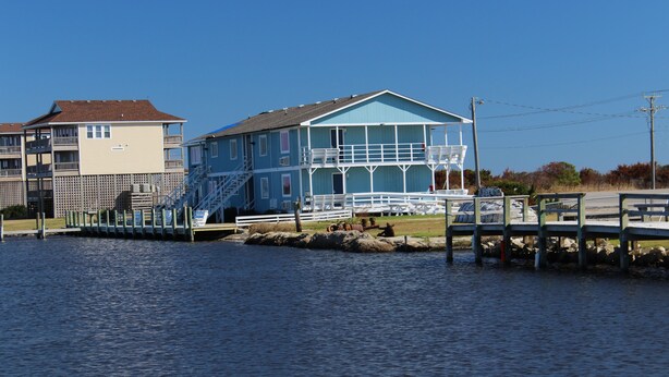 A waterfront property with a large blue house featuring a balcony and a staircase leading to the entrance. - Fin 'n Feather Waterside Inn By Kees Vacations (Nags Head)