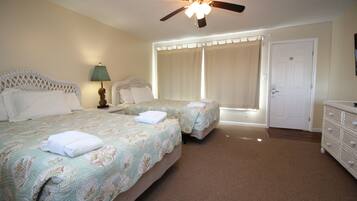 A hotel room with two beds, a ceiling fan, a nightstand with a lamp, a dresser, and a door.