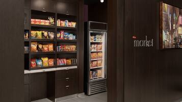 A snack display with various chips and snacks, a refrigerator with beverages, and a wall with a framed picture.
