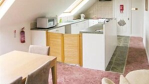 A compact kitchen with a dining area, a fire extinguisher, and a visible door. - The Gables Guest House (Lincoln)