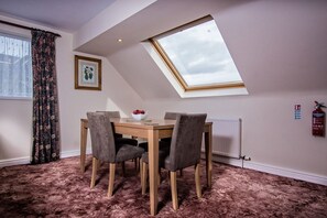 A dining area with a table and chairs, a window with a view, a framed picture on the wall, and a fire extinguisher.