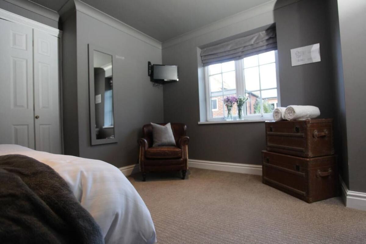A bedroom with a bed, a chair, a dresser, a window with a view, and a mirror.