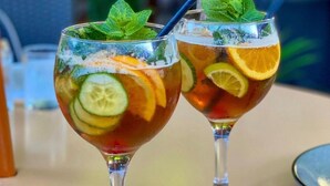 Twee glaasjes ijsthee met fruitschijfjes en muntblaadjes.