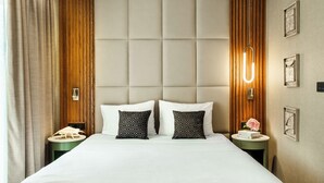 Une chambre d’hôtel avec un grand lit, deux tables de chevet, une tête de lit en bois et un luminaire fixé au mur.