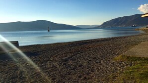 Un littoral rocheux, une mer calme, des montagnes lointaines et un phare.