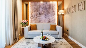 Un salon moderne avec un canapé gris, une table basse ronde sur laquelle on trouve des fruits et des verres à vin, un grand tableau abstrait accroché au mur et un lampadaire.