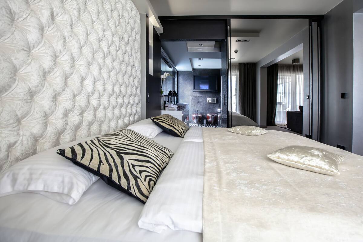 Een moderne hotelkamer met een groot bed, een gestoffeerd hoofdeinde en uitzicht op de badkamer en keuken.