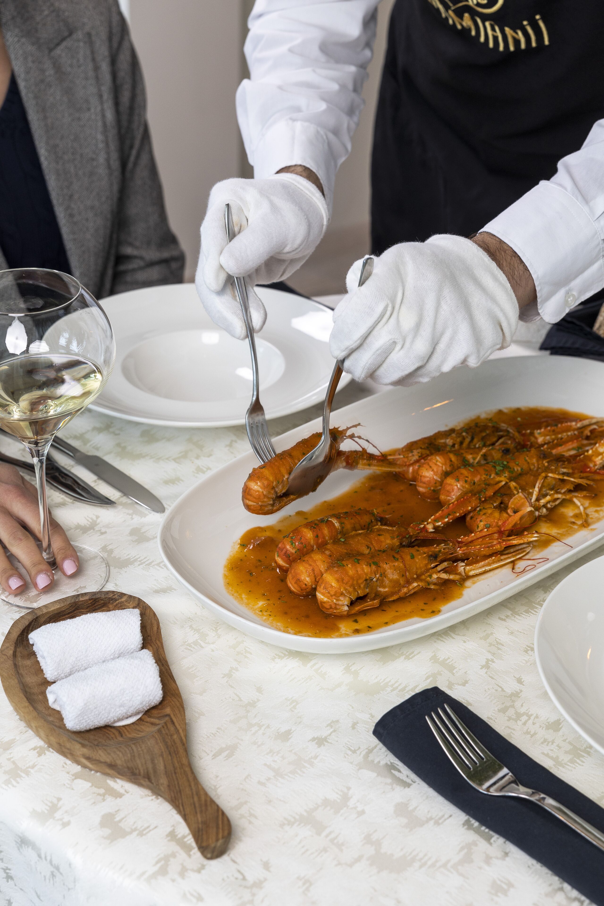 A dining table with a plate of seafood, a wine glass, and a wooden napkin holder.