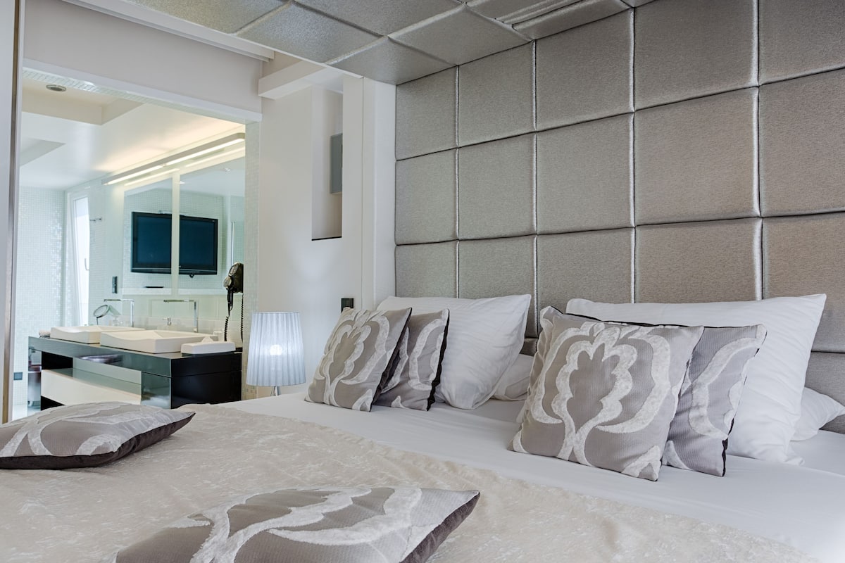 Een moderne hotelkamer met een groot bed, een ingebouwde televisie, een badkamer met spiegel en een nachtkastje.