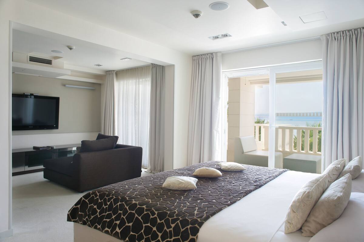 Een hotelkamer met een bed, een slaapbank, een televisie en een balkon met uitzicht.