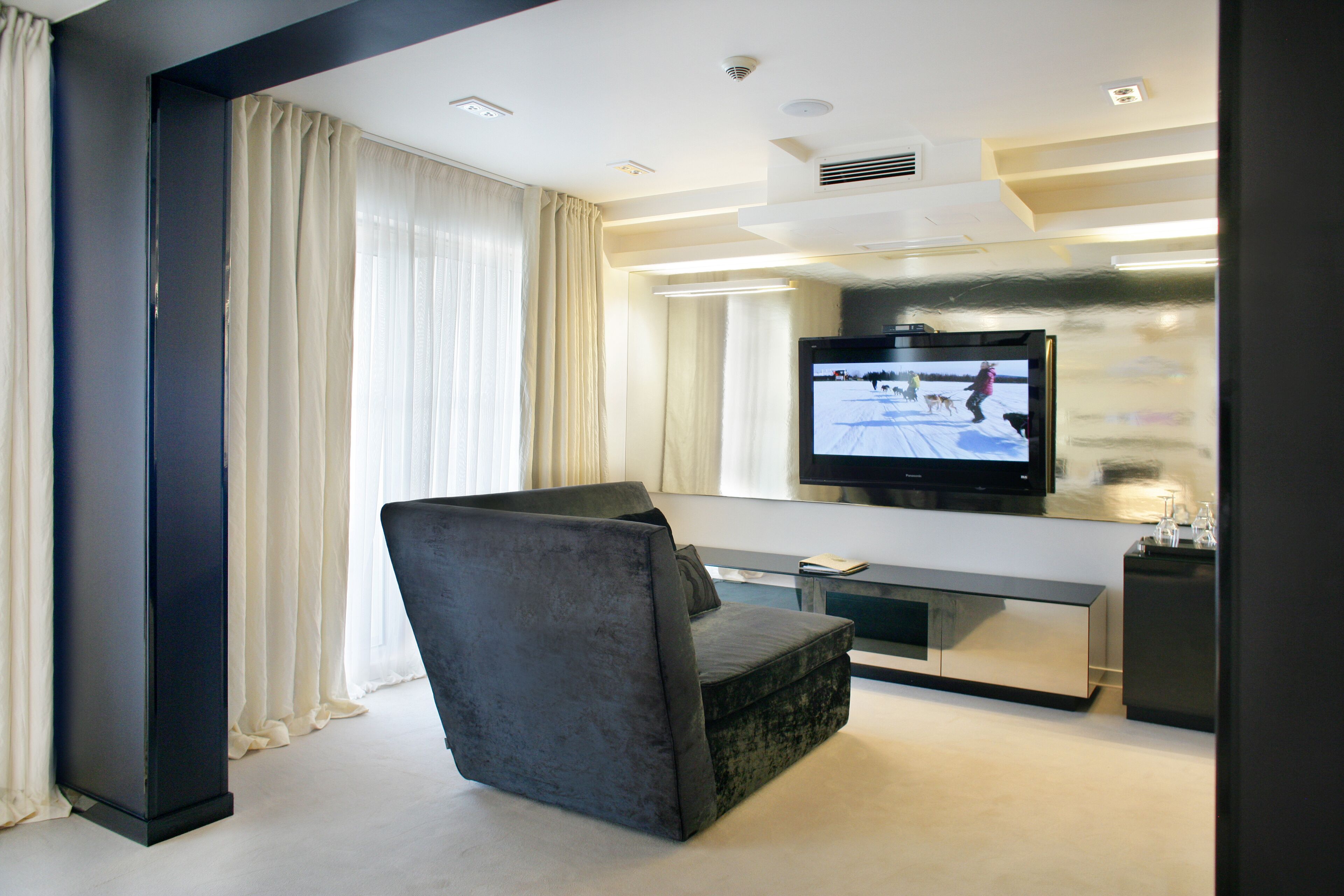 A modern living room with a grey sofa, a flat-screen TV mounted on the wall, and a minimalist design.