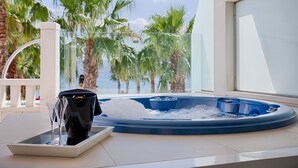 Een hottub met glazen omheining, een champagnefles en een glas op een dienblad, met uitzicht op palmbomen en een wateroppervlak.