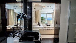 Een moderne hotelkamer met een grote spiegel, een zwart bad en een balkon met uitzicht op zee.