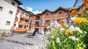 A multi-story building with balconies, outdoor seating, and a garden with flowers. - Hotel Majorka (Andalo)