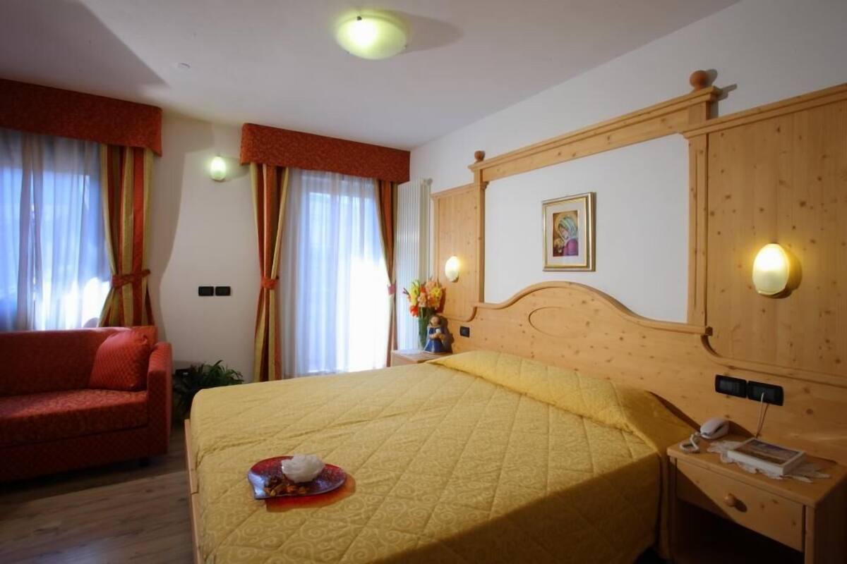 A hotel room with a bed, a wooden headboard, a nightstand, a red sofa, and a painting on the wall.