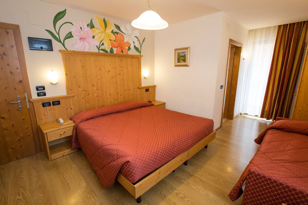 A bedroom with a wooden bed, a nightstand, a wall-mounted light, and a floral mural.