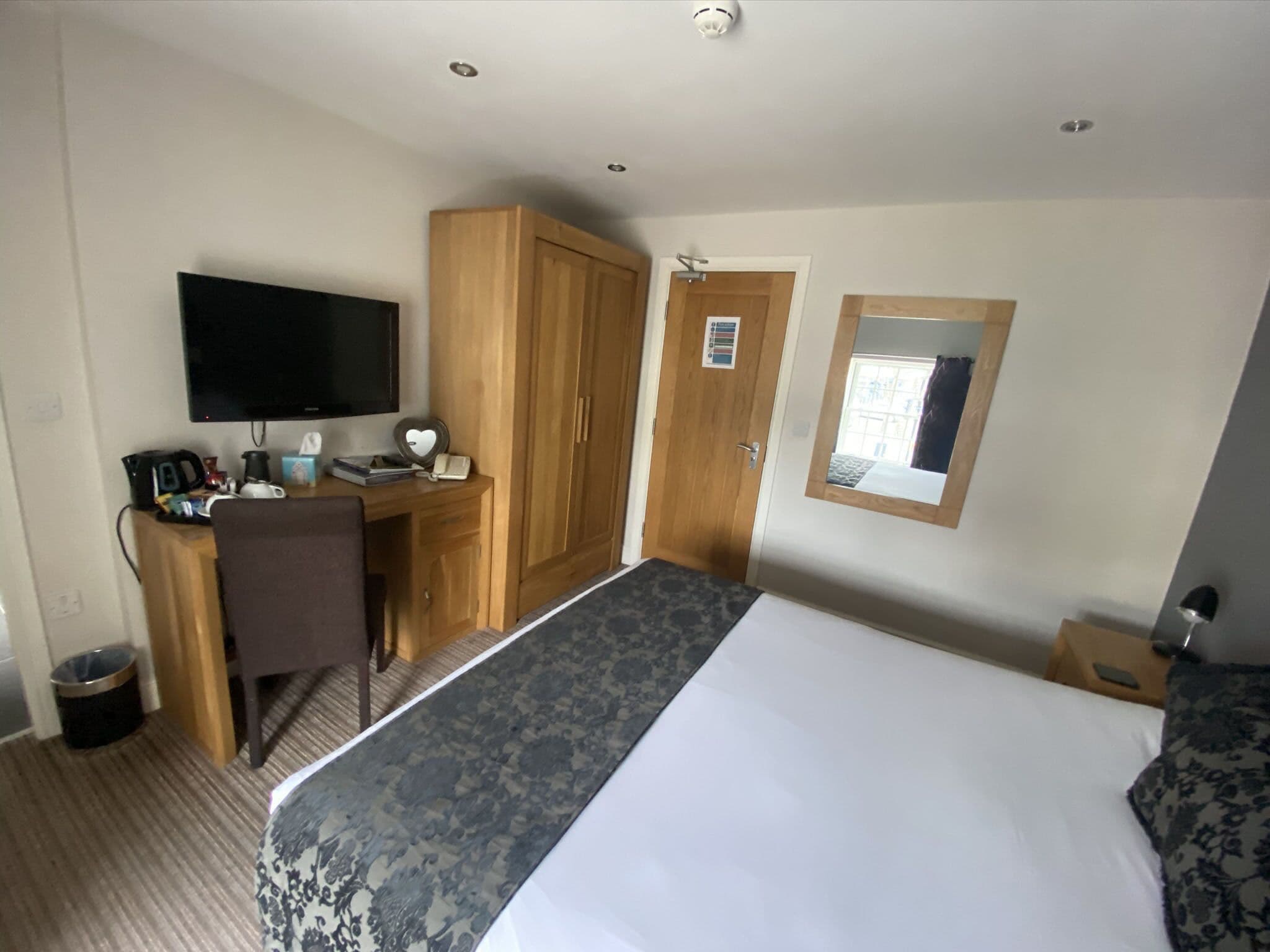 A hotel room with a bed, a desk with a TV, a wardrobe, and a small window.