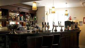 A bar area with a counter, bar stools, and a variety of bottles and glasses.