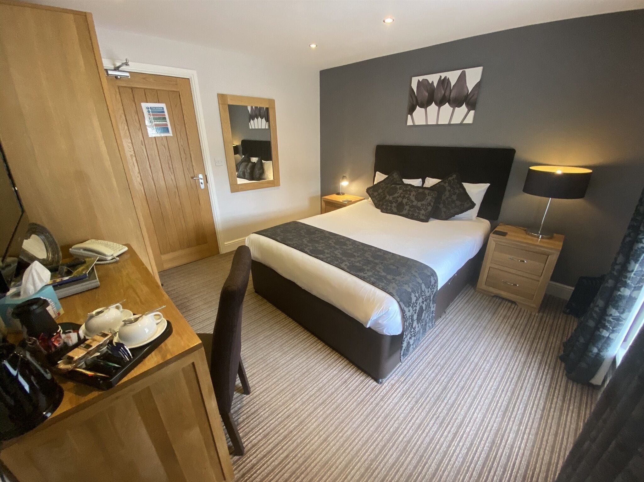 Une chambre d’hôtel comprenant un lit, des tables de chevet, un bureau avec une chaise, un miroir et une œuvre d’art accrochée au mur.