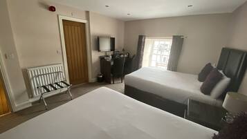 A hotel room with two beds, a desk, a chair, a TV, and a window with curtains.