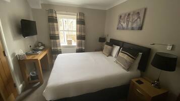 A neatly arranged bedroom with a bed, bedside tables, a television, and a painting on the wall.