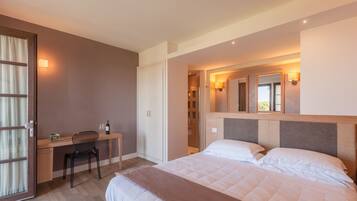 A hotel room with a bed, a desk, and a chair. There is a wardrobe, a mirror, and a window.