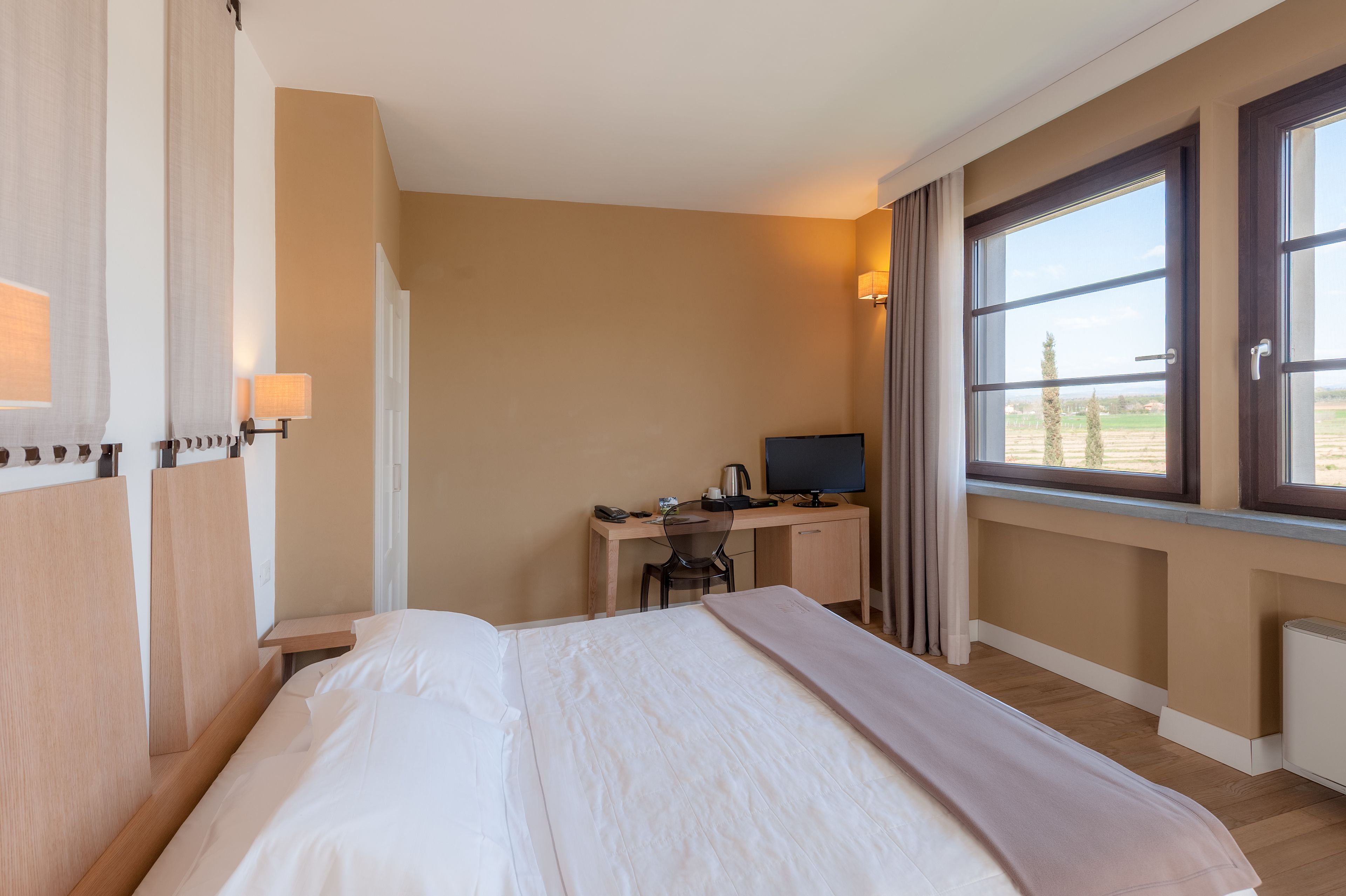 Habitación de hotel con cama, escritorio y vista al campo.