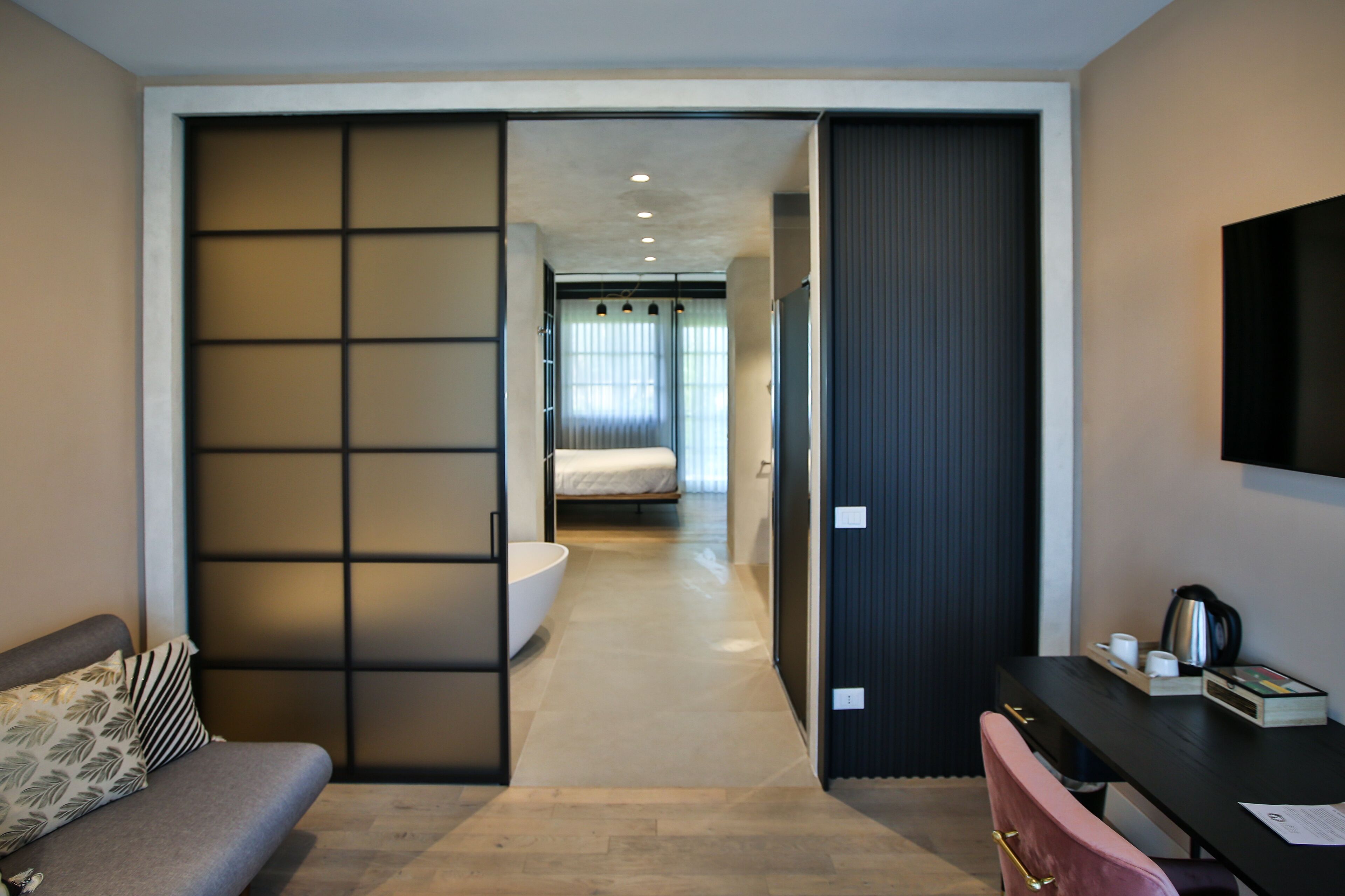 Habitación de hotel moderna con puerta corredera que da al baño, un escritorio con silla y una cama al fondo.
