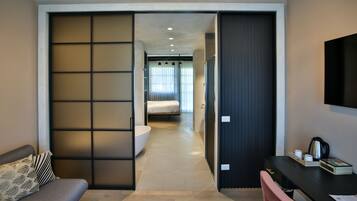 Habitación de hotel moderna con puerta corredera que da al baño, un escritorio con silla y una cama al fondo.