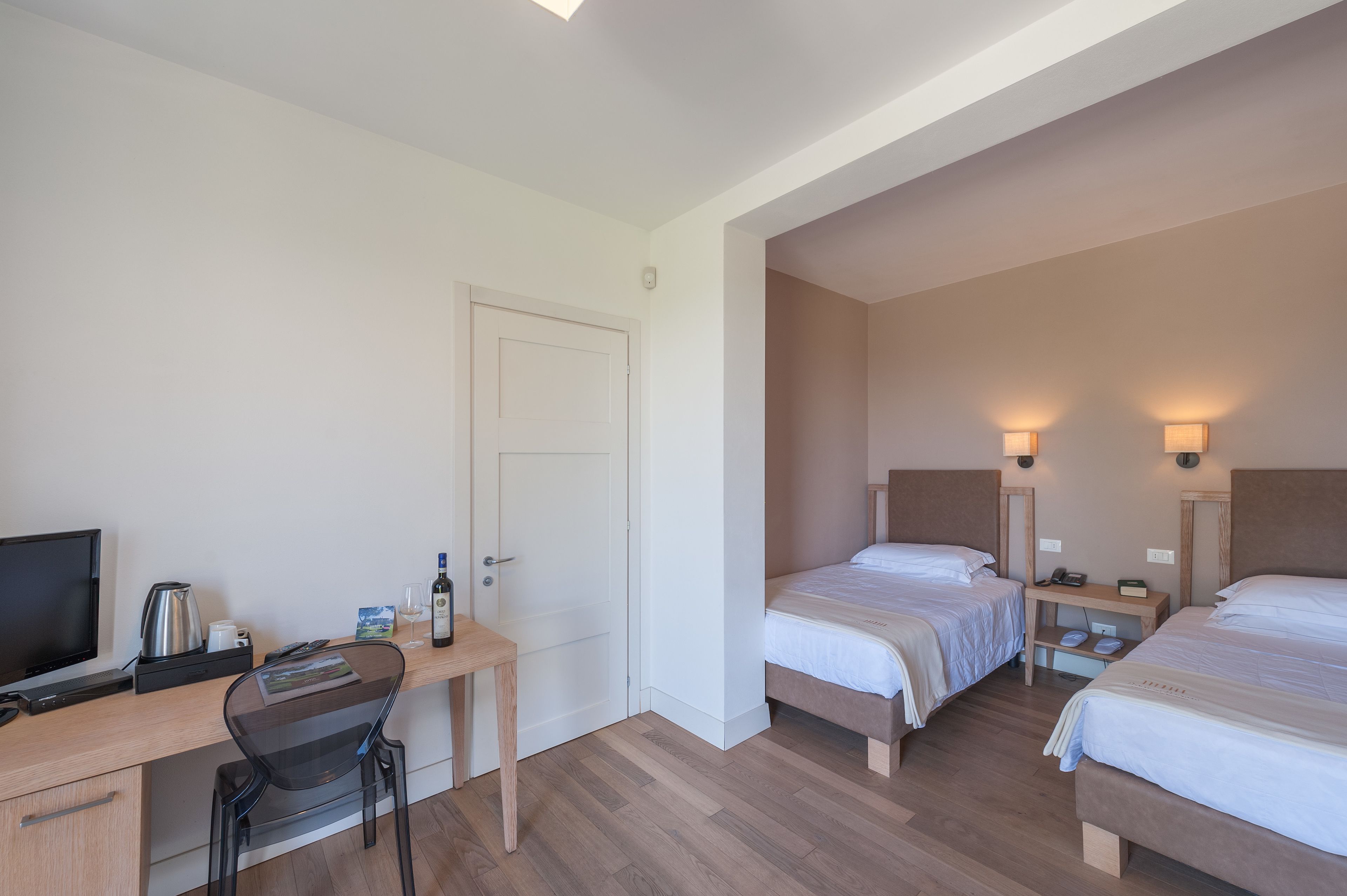 Habitación de hotel con dos camas, un escritorio con computadora, una silla, televisor y cafetera.