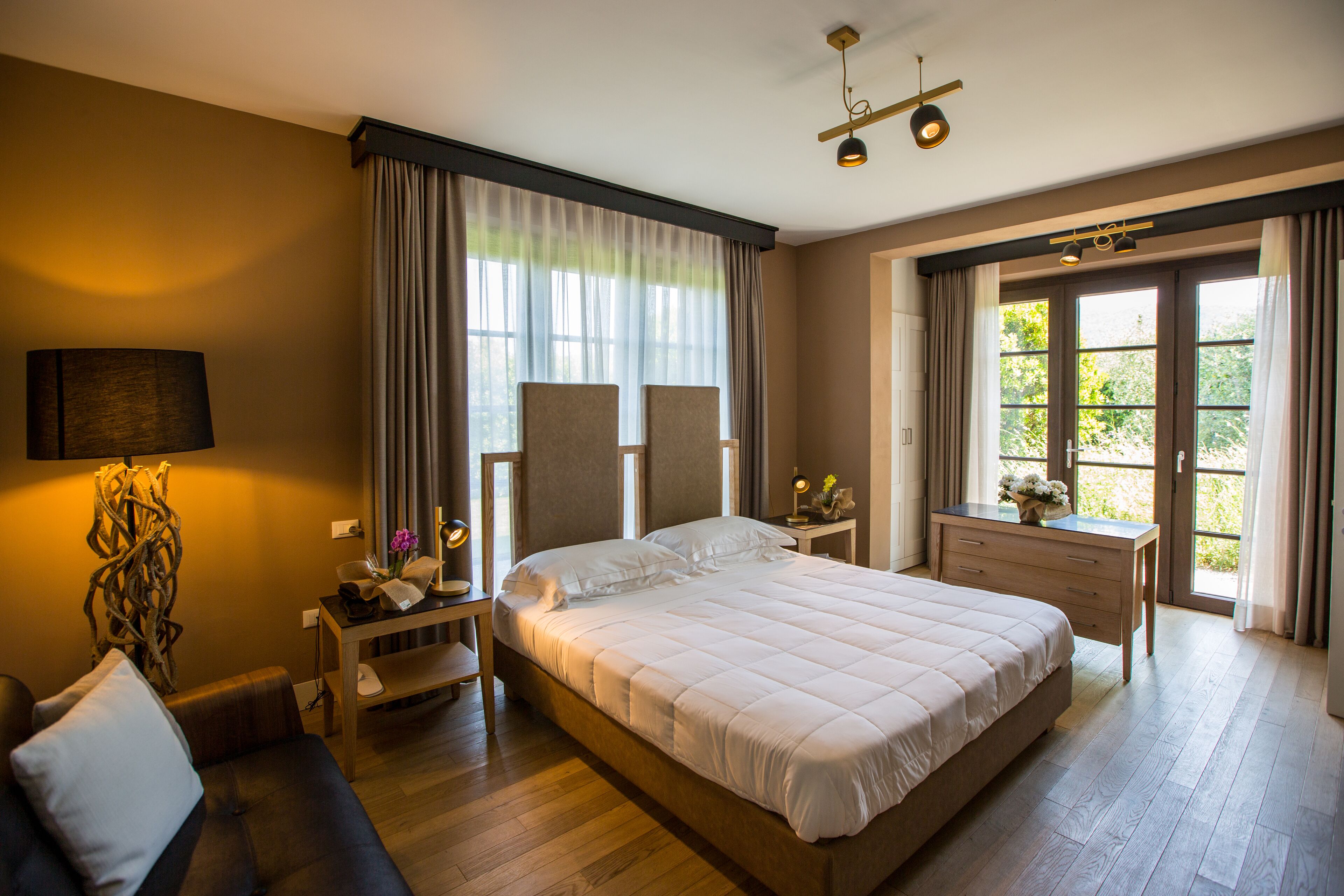 A spacious bedroom with a large bed, a bedside table with a lamp, a dresser, and a window with curtains.