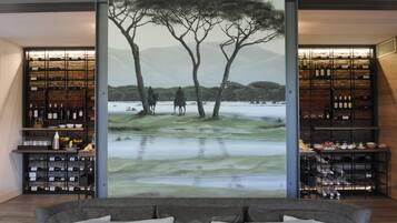 Une pièce décorée d’une grande fresque représentant un paysage, avec des étagères à vin et un canapé.