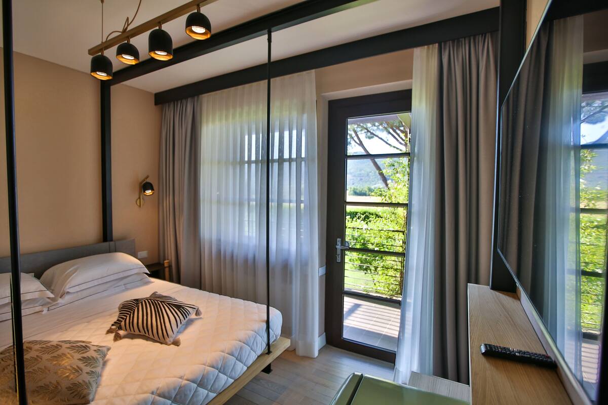 Un dormitorio moderno con cama, cortinas, ventana y vistas a zonas verdes.