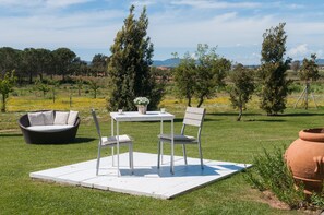 An outdoor seating area with a table and chairs, surrounded by a grassy field and trees.