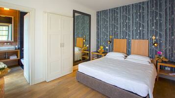 Een slaapkamer met een groot bed, een houten nachtkastje, een spiegel, een dressoir, en een badkamer zichtbaar door een geopende deur.