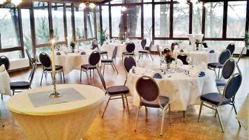 A banquet hall with round tables, chairs, and large windows.