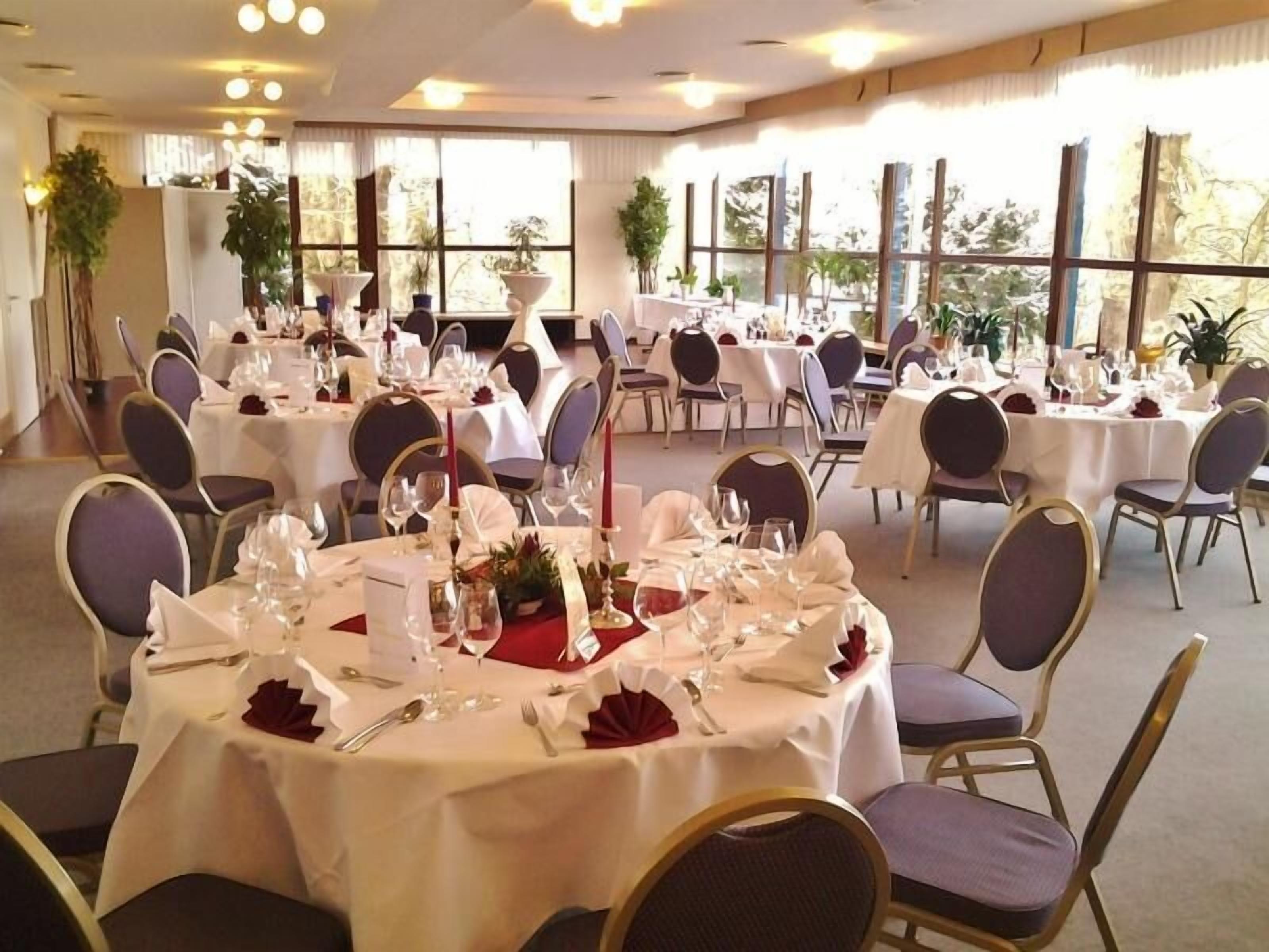 A banquet hall with round tables set for dining, featuring white tablecloths, red napkins, and gold-rimmed chairs.